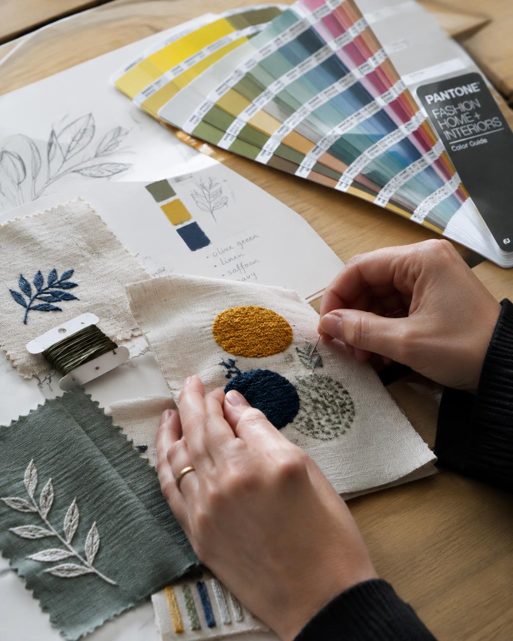 Mains d'une designer travaillant sur des échantillons de broderie à côté d'un nuancier Pantone
